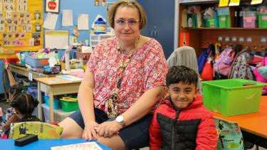 Instructional Support Staff Appreciation Woman with short hair, wearing glasses and floral shirt sits next to young kindergarten boy in a classroom