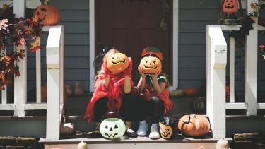Kids dressed up for Halloween Little children in Halloween costumes sitting on steps holding pumpkins in front of their faces