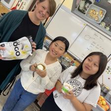 Two students with cups of yogurt. Teacher holding bag of yogurt.